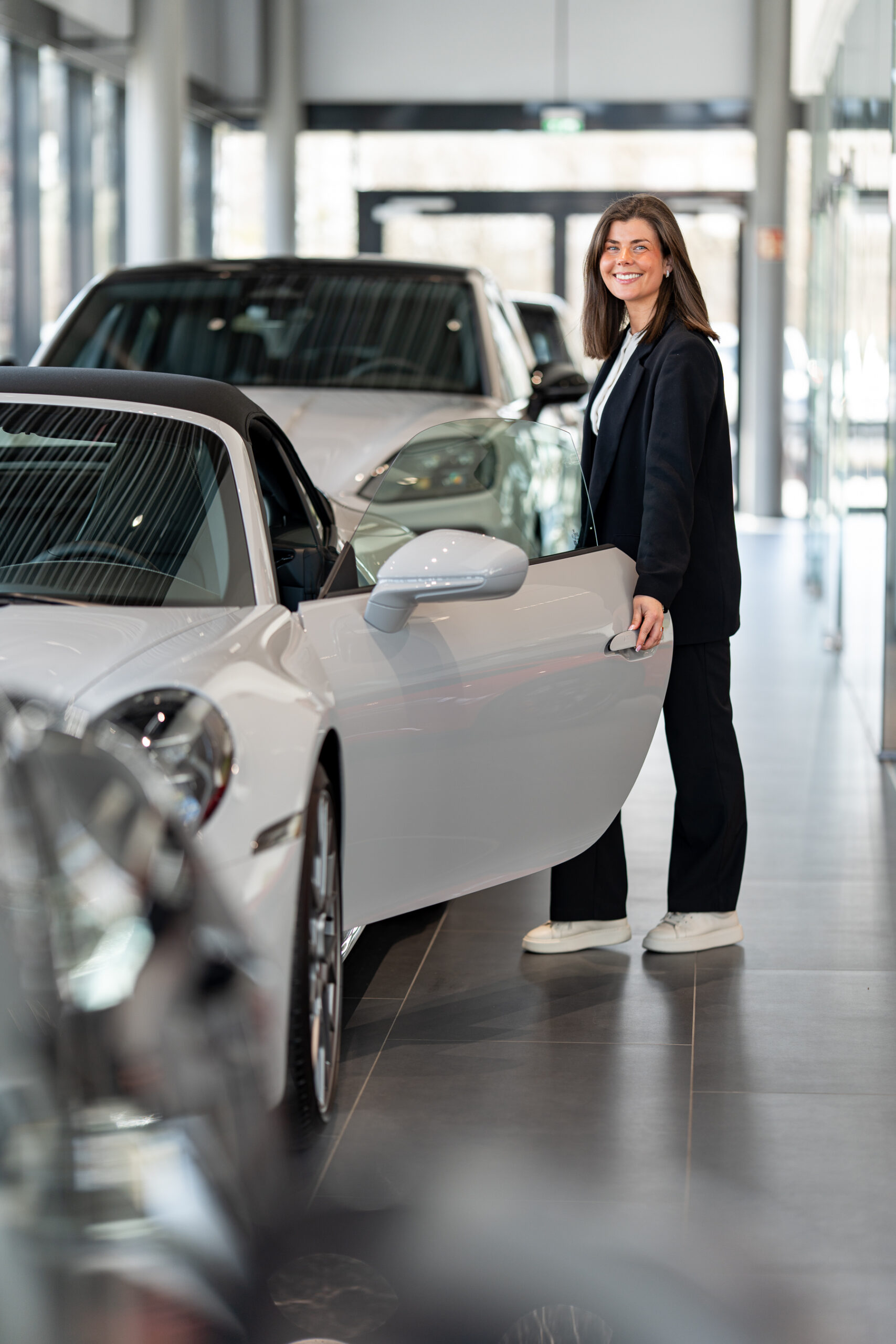 Frau im Autohaus-Showroom neben weißem Sportwagen, Businessportrait im Unternehmensumfeld für Bremer Firmen