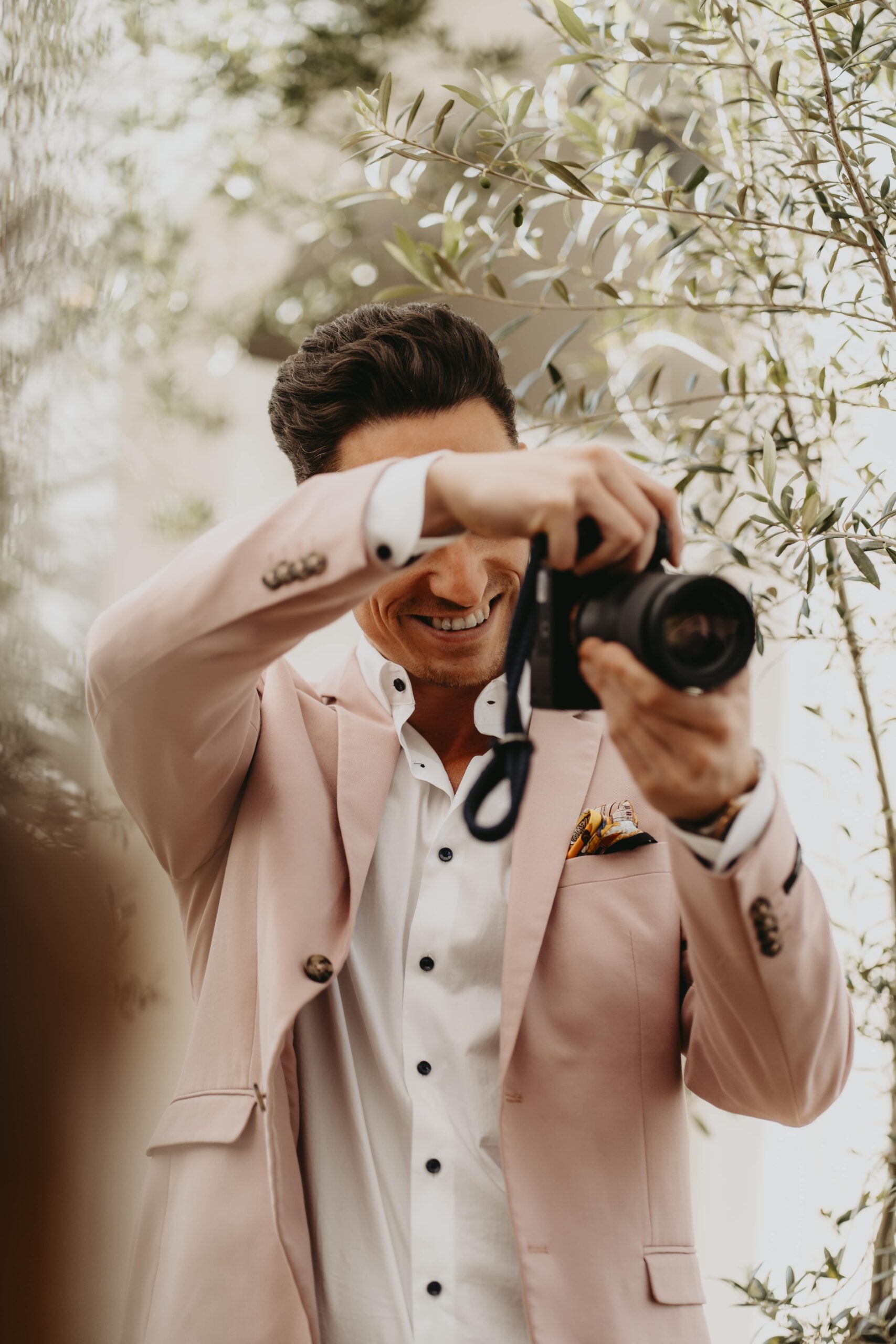 Fotograf Julien Jones im rosa Sakko mit Kamera vor Olivenzweigen, Businessfotograf für Bremen