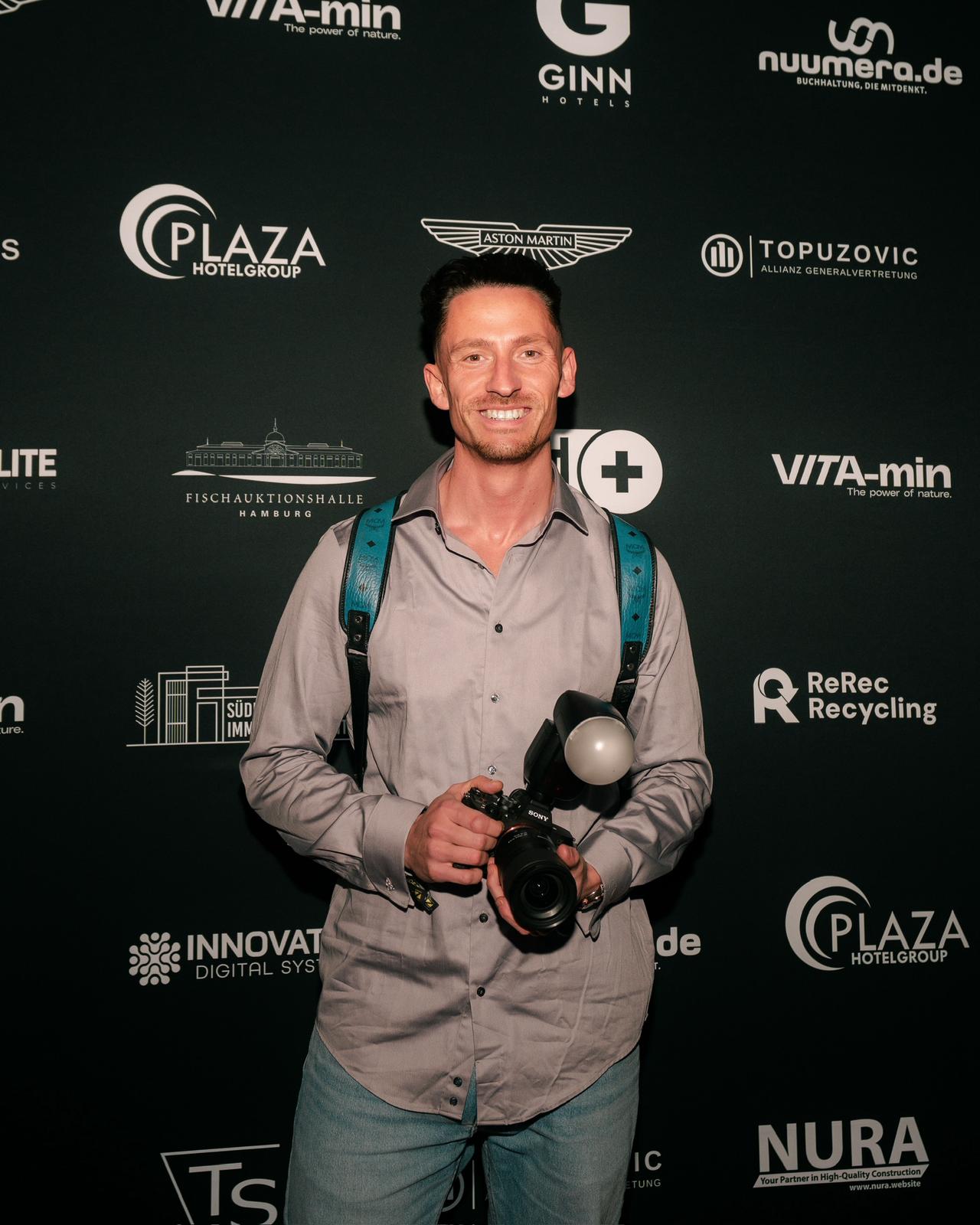 Julien Jones mit Kamera vor einer Sponsorenwand, Eventfotograf für Lübeck bei der Arbeit